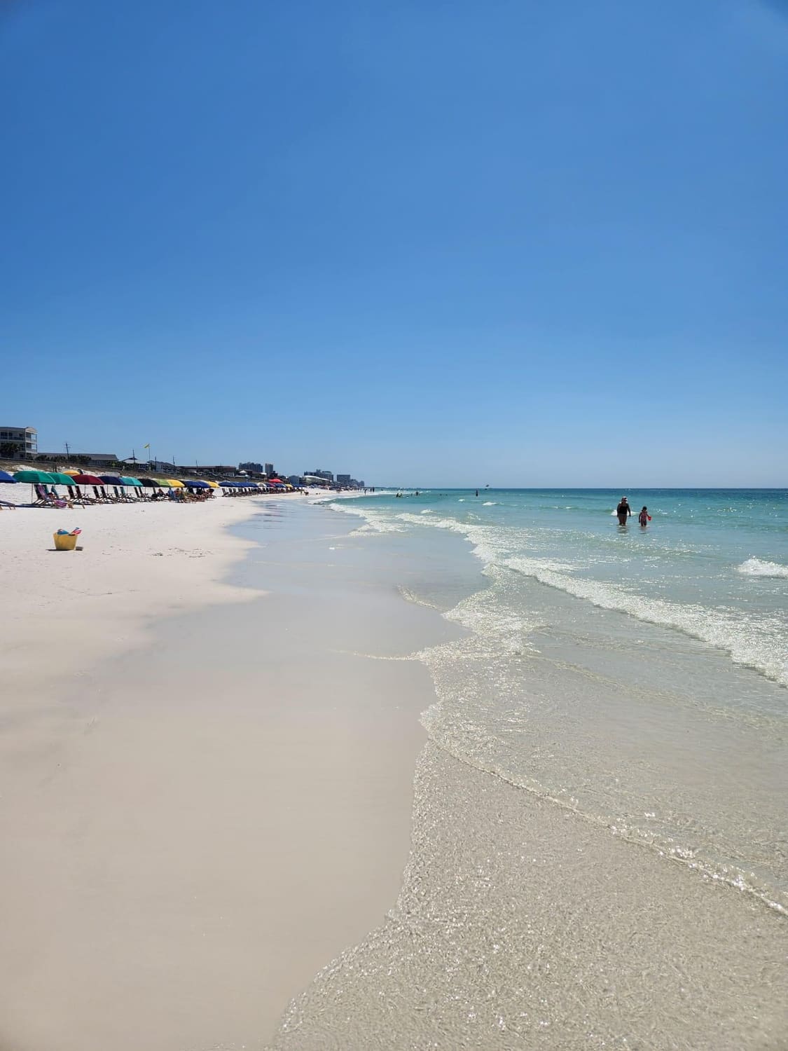 Pristine white sand beach with turquoise water, beach umbrellas, and swimmers on a clear day