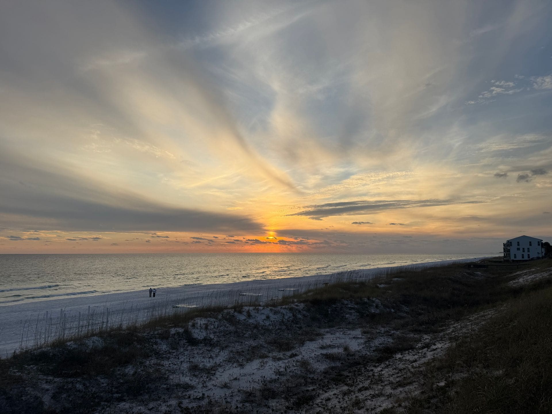 Sunset over ocean beach with sand dunes, beach grass, and white house on right