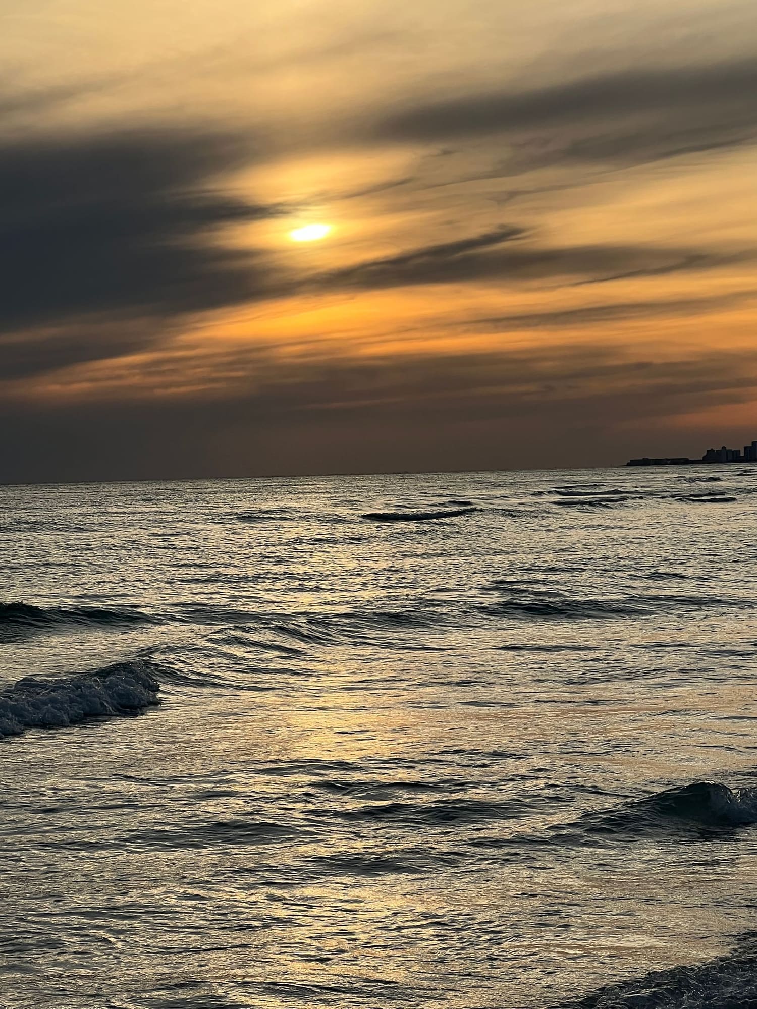 Golden sunset over ocean waves with cloudy sky and distant shoreline