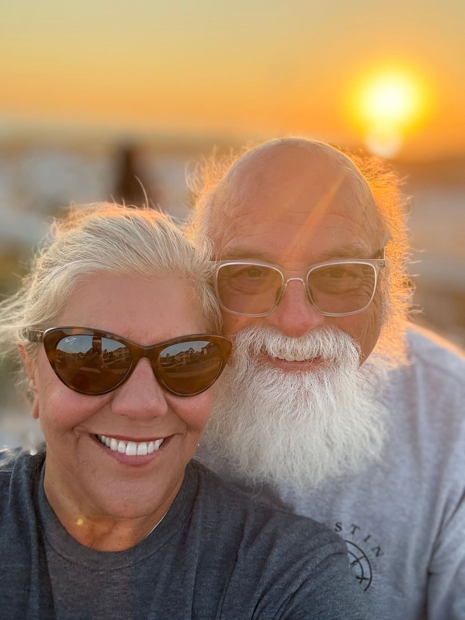 Two people smiling at sunset with ocean and blurred buildings in background