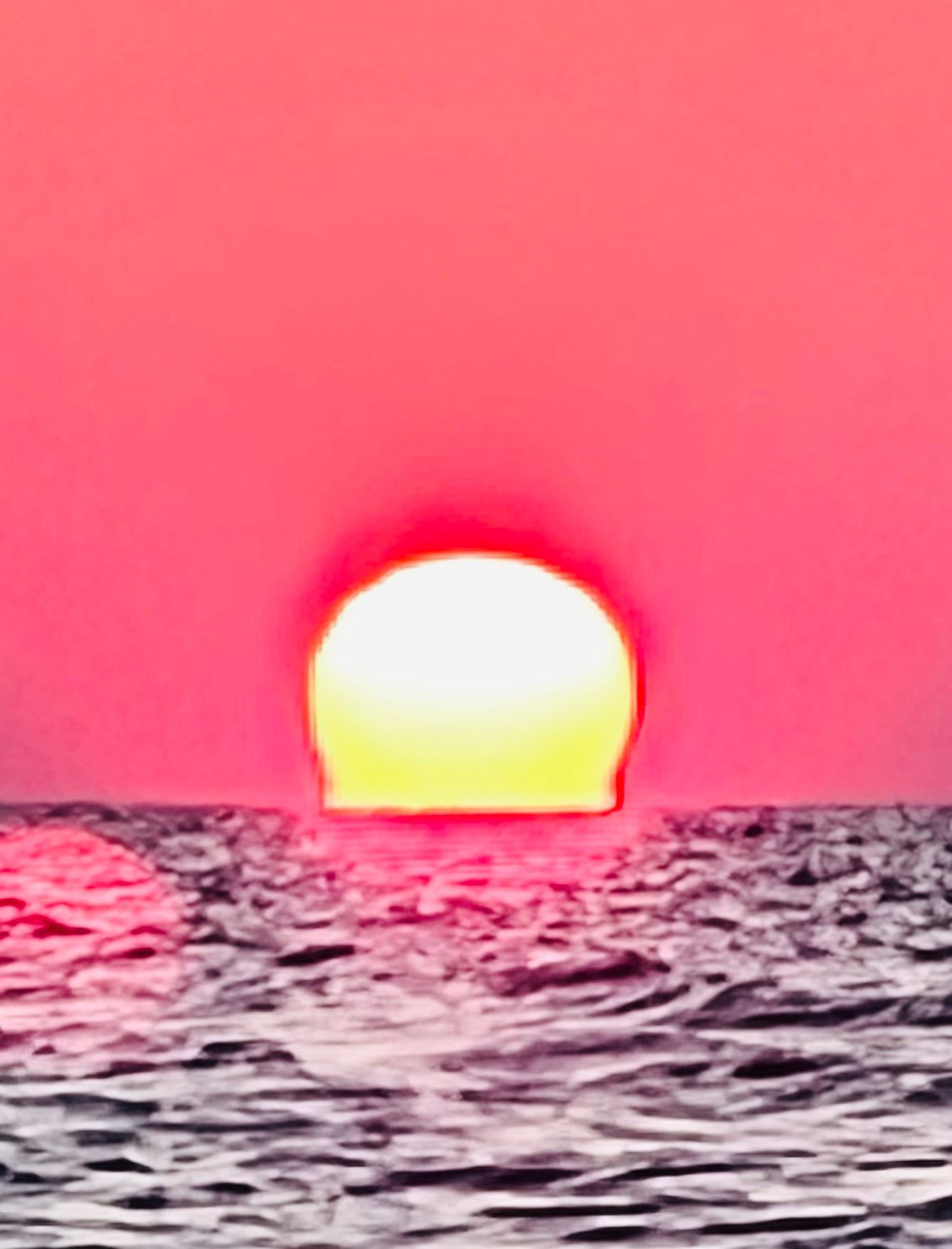 Glowing sun setting over rippled desert landscape against pink sky