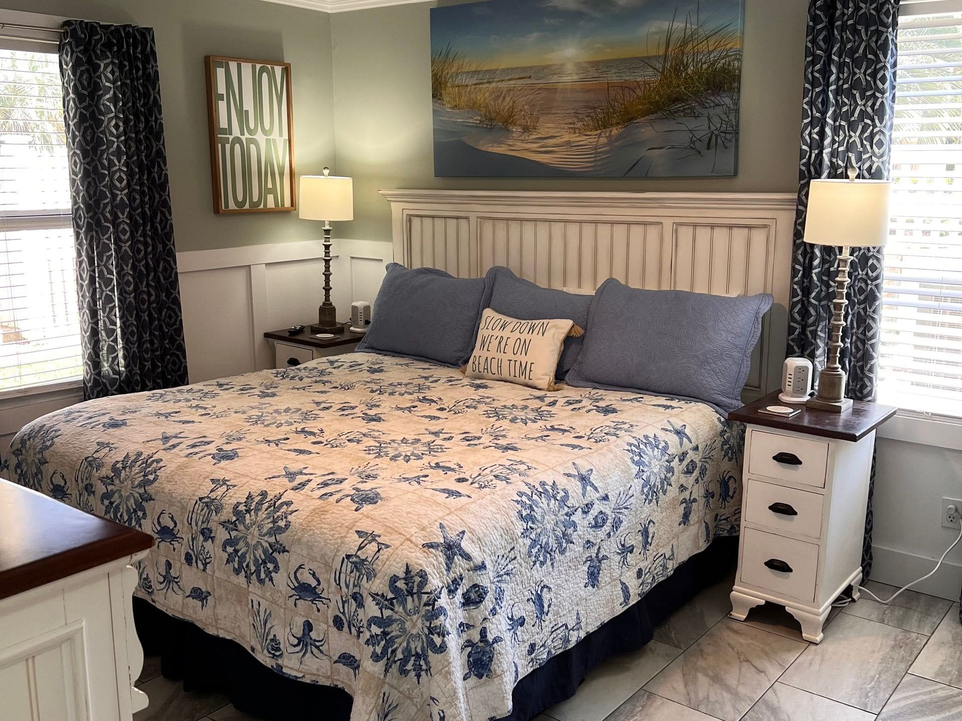 Coastal-themed master bedroom with beige and blue décor, beach landscape artwork, and nautical bedding