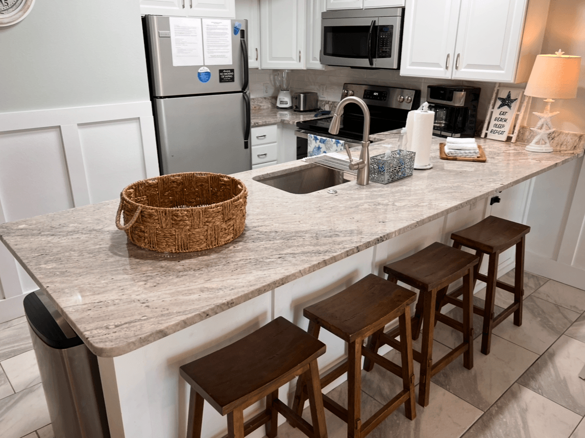 Modern kitchen with white cabinets, stainless steel appliances, and granite countertop with four wooden bar stools