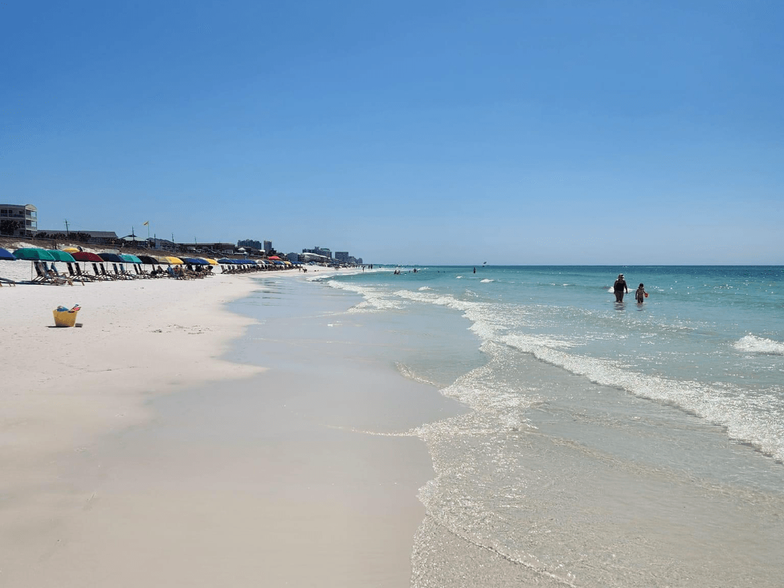 Pristine sandy beach with colorful beach chairs, turquoise waves, and swimmers enjoying the clear water