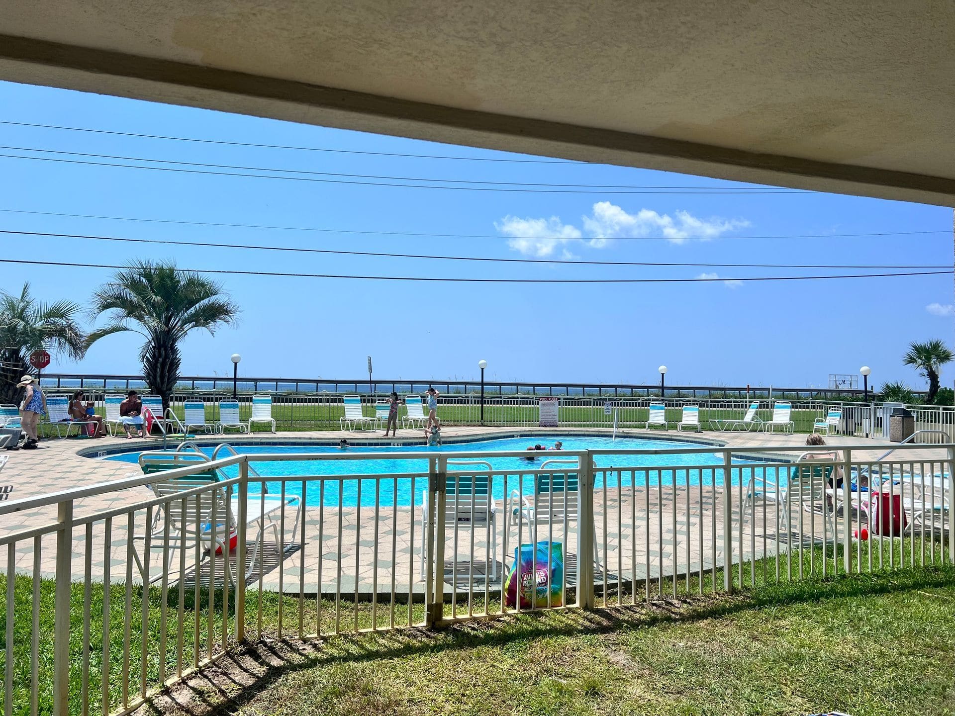 Beachfront swimming pool with blue water, metal railings, lounge chairs, and ocean view beyond