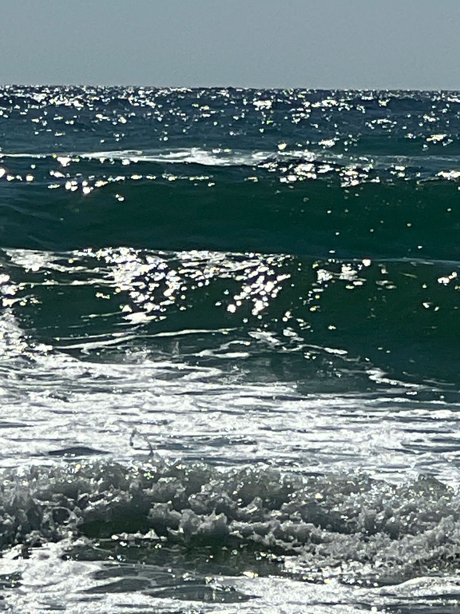 Ocean waves with white foam and sparkles of sunlight on blue-green water